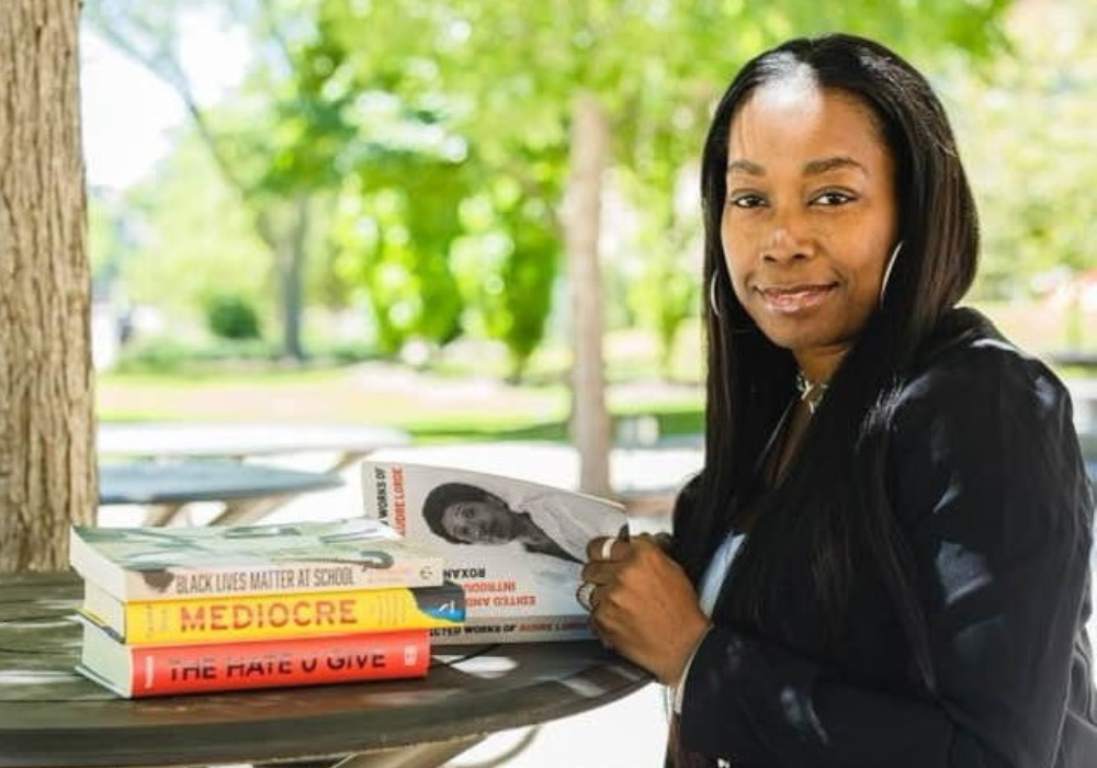 Woman sits at table with stack of books