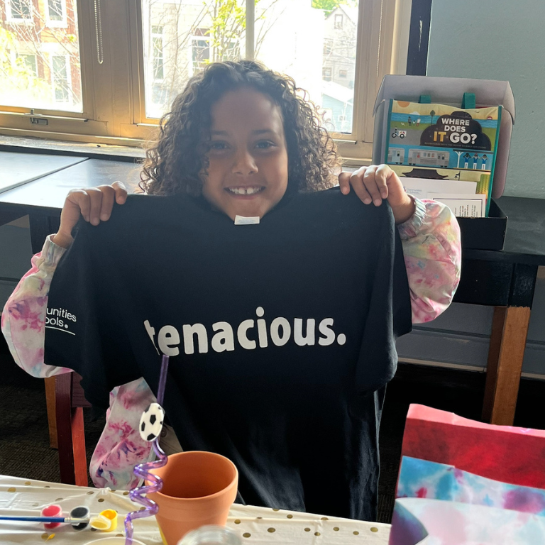 Student holds up "tenacious" T-shirt